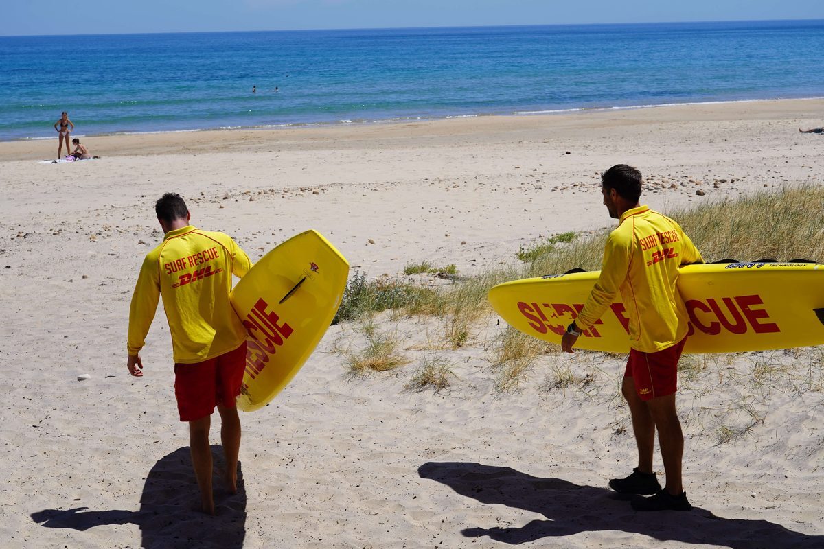 Two Life Saving Victoria volunteers carrying rescue boards onto the beach
